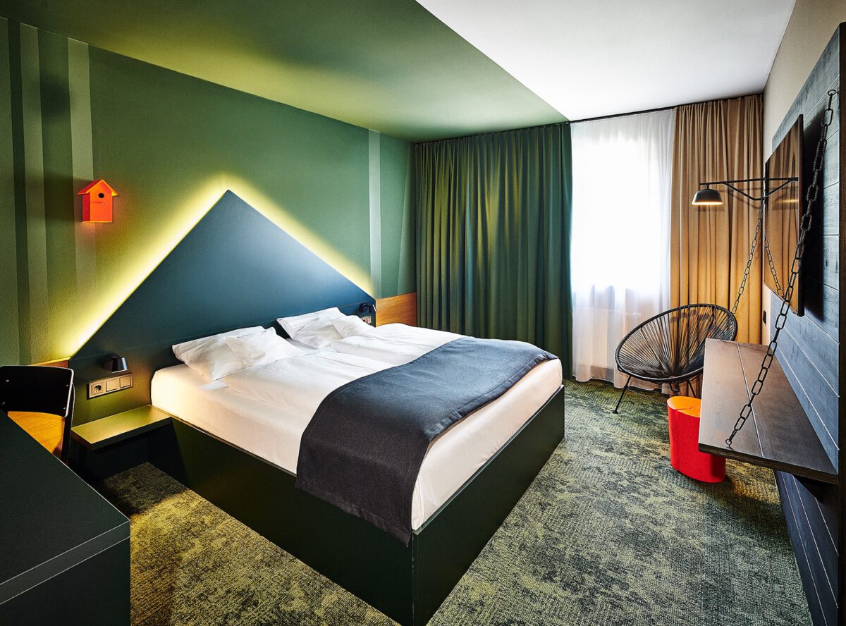 Hotelzimmer mit grünem Farbkonzept, Doppelbett und geometrischer Wandgestaltung im Hospitality Design