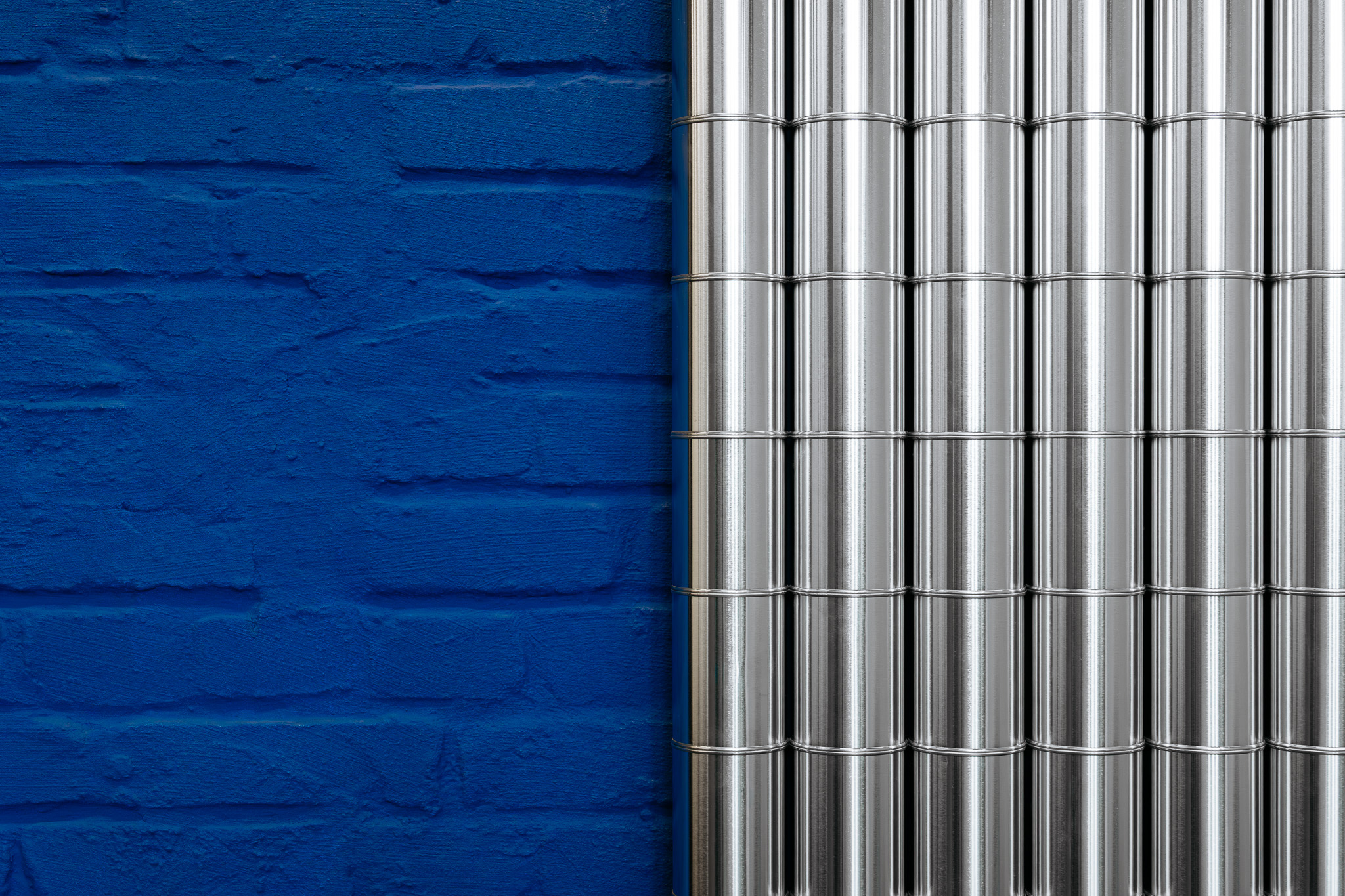 Detail einer blau gestrichenen Backsteinwand neben vertikaler glänzender Metallverkleidung im Bildungscampus