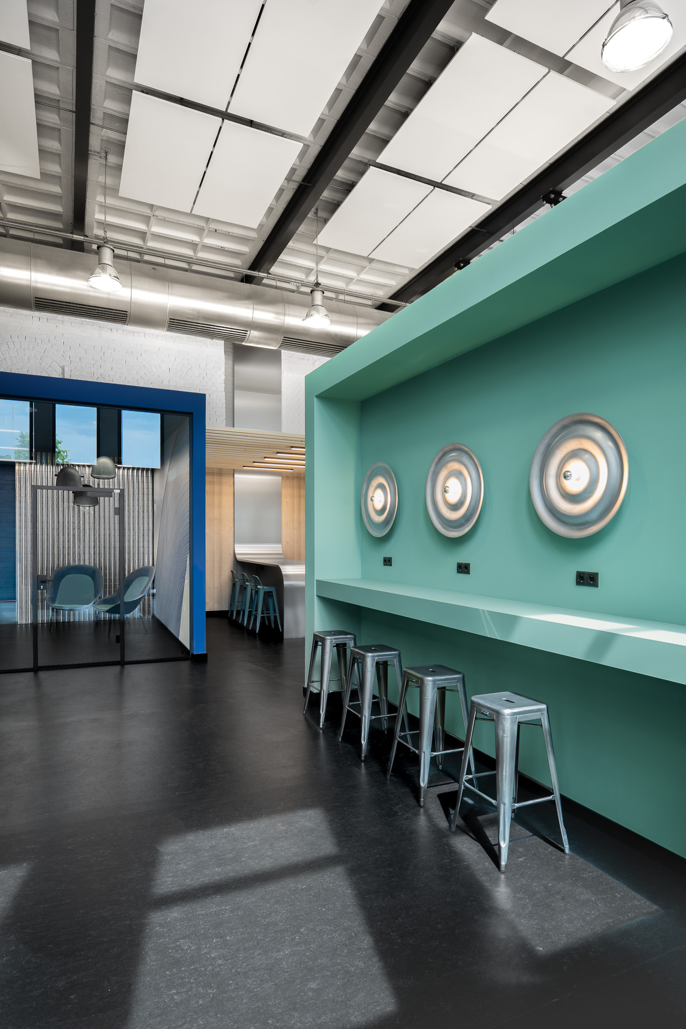 Offene Innenarchitektur des Bildungscampus mit mintfarbenem Raumkörper, runden Metallleuchten, blauem Seminar-Cube und Metallhockern