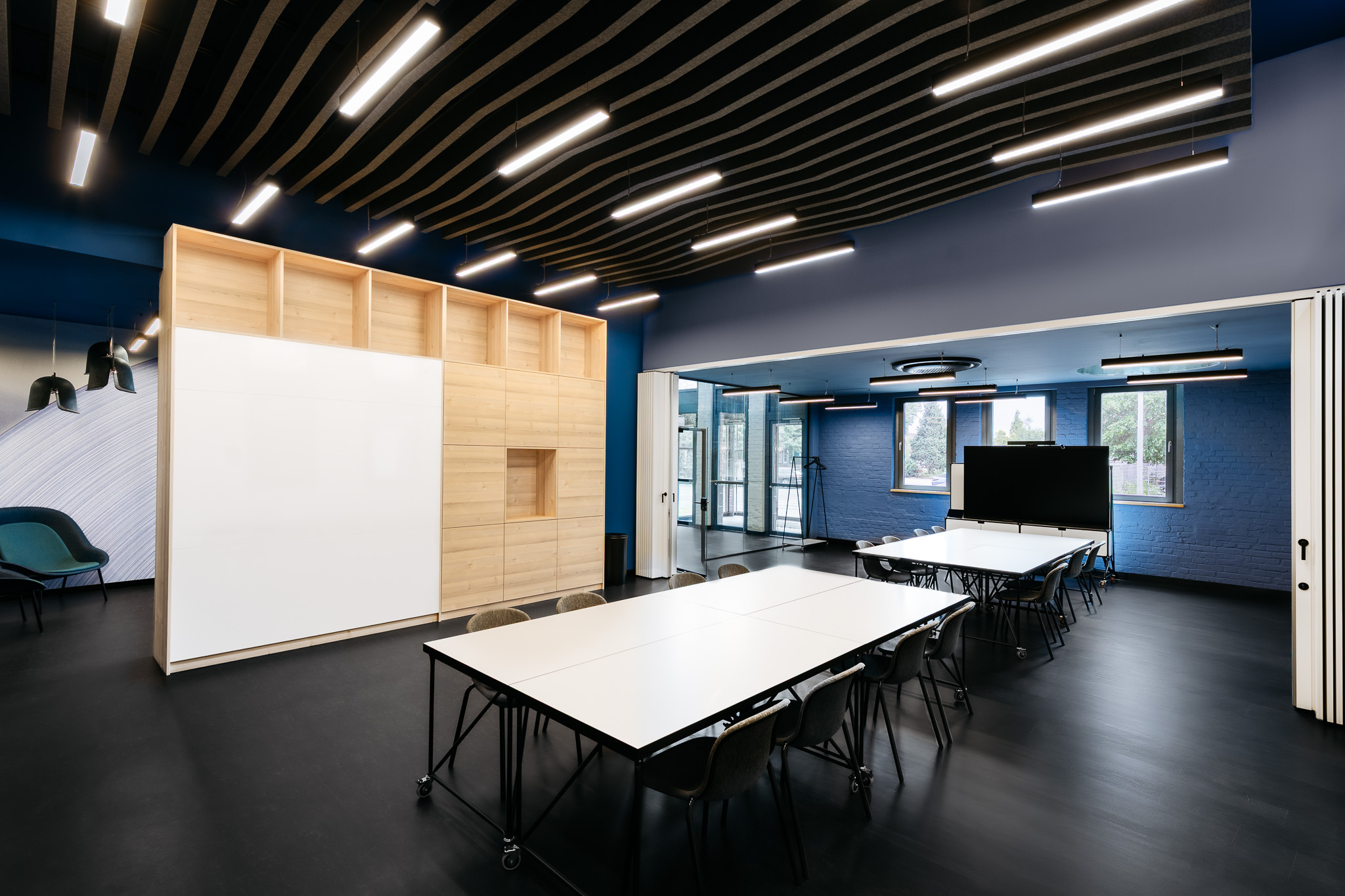 Flexibler Konferenzraum im Bildungscampus mit mobilen Seminartischen, Falttrennwand, Holz-Einbau und schwarzer Lamellendecke