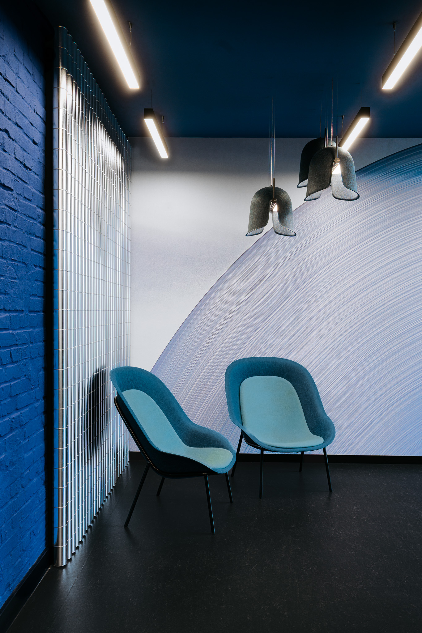 Informeller Besprechungsbereich mit blauer Backsteinwand, Metallverkleidung, Sesseln und Pendelleuchten